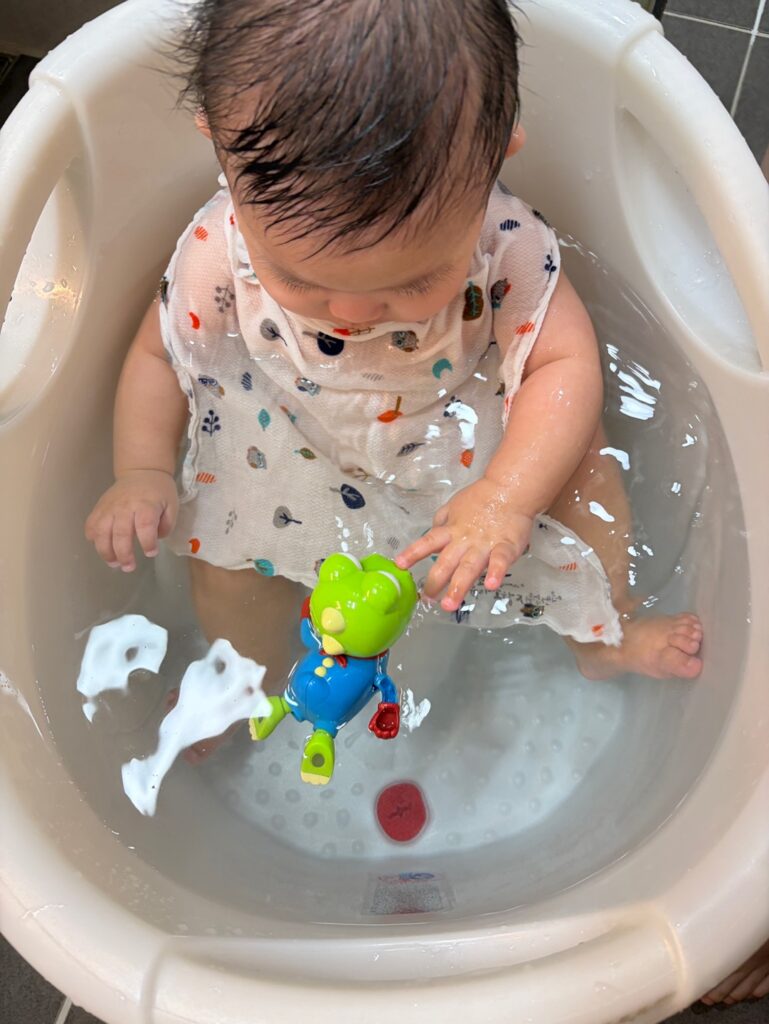 목욕 중 6개월 아기가 수영하는 크롱 장난감을 손으로 조심스럽게 만지는 모습